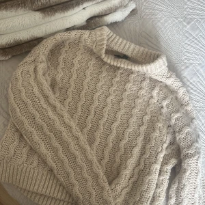 Beige stickad tröja - Mysig beige stickad tröja med ett vågigt mönster. Perfekt för kyliga dagar med sin varma och bekväma design. Tröjan har långa ärmar och en rund halsringning.