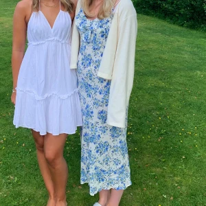 Blommig långklänning med volangdetalj från Mango - Säljer en vacker långklänning med blått blommönster på vit bakgrund från Mango. Klänningen har smala axelband och en söt volangdetalj vid halsringningen. Perfekt för sommarens alla tillfällen! Storlek L men passar mig som är S/M 🥰