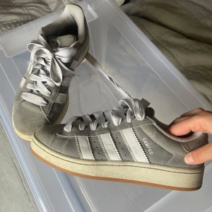 Grå Adidas Campus sneakers - Säljer ett par stilrena grå Adidas Campus sneakers med klassiska vita ränder och snörning. Snygga nu till våren och sommaren! 🌸
