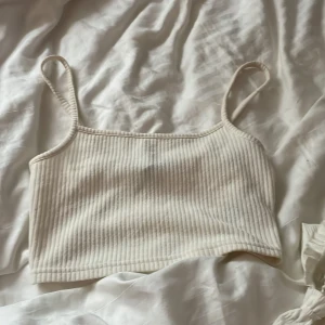 Vit ribbad linnetopp från Divided - Säljer en stilren vit ribbad linnetopp från Divided. Toppen har smala axelband och en croppad passform, perfekt för varma dagar. Enkel och snygg att matcha med olika outfits.