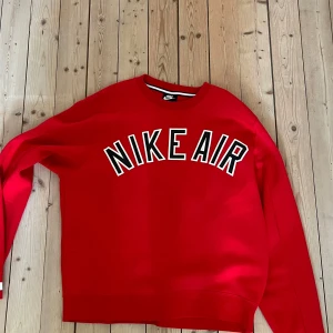 Röd sweatshirt från Nike Air - Säljer en röd sweatshirt från Nike Air med stor vit och svart logga på bröstet. Tröjan har rund halsringning och långa ärmar. Perfekt för en sportig och avslappnad stil.