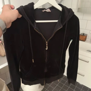 Svart hoodie Juicy Couture - Säljer en klassisk svart hoodie i mjuk velour från Juicy Couture. Jackan har dragkedja framtill, huva med snören och ribbade muddar. Stl S