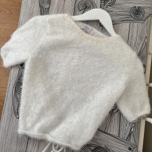 Vit stickad topp med knytkrage - Supermjuk och fluffig vit stickad topp från NA-KD med korta ärmar och söt knytkrage. Perfekt för dig som gillar en enkel men ändå unik stil. Lätt att matcha med både jeans och kjol.