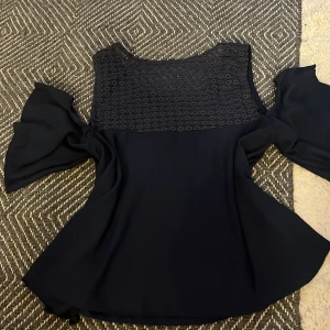 Svart blus med spets och volangärmar - Säljer en svart blus med vacker spets upptill och vida volangärmar. Blusen har en elegant och luftig design med detaljerad spets över bröstet och axlarna. Perfekt för dig som vill ha något stilrent men ändå med det lilla extra.