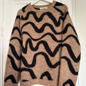 Tröja i ull och alpacka från Carin Wester - Säljer en beige stickad tröja från Carin Wester med svarta vågiga mönster. Tröjan har rund halsringning och långa ärmar. Materialmix med ull och alpacka för extra mjuk känsla. Kvalitetströja, mycket sparsamt använd!