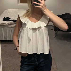 Vit volangtopp zara - Säljer en söt vit topp med bred volangkrage och ärmlös design. Toppen har en lätt A-linjeform och knäppning bak i nacken. Endast använda fåtal ggr är i nyskick! Från zara storlek xs