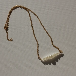 Guldhalsband med pärlor - Snyggt halsband med tunn guldfärgad kedja och vita pärlor i olika storlekar framtill. Perfekt accessoar för att lyfta din outfit med en elegant touch.