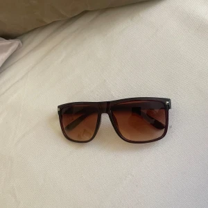 Bruna solglasögon med fyrkantig form - Snygga solglasögon med bred, fyrkantig båge i mörkbrunt plastmaterial och bruna tonade glas. Perfekt accessoar för soliga dagar och ger en cool look. Liknar rayban glasögon.