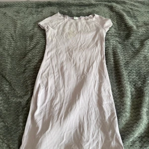 Ljuslila ribbad klänning från Lindex - Ljuslila ribbad klänning från Lindex i enkel och rak modell. Kortärmad med rund halsringning och diskreta volangdetaljer vid halsen. Perfekt för en avslappnad stil under varmare dagar.