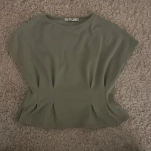 Grön topp från nakd  - Säljer en topp från nakd korta ärmar och rund halsringning. Toppen har en rak passform och diskreta veckdetaljer.