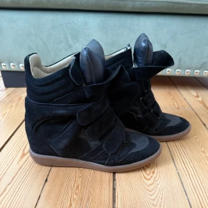 Svarta sneakers med kilklack från Isabel Marant - Säljer ett par svarta sneakers från Isabel Marant med kilklack (5 cm) och breda kardborreband, som tyvärr inte kommer till användning längre. Skorna är i mocka och skinn med gummisula och har en sportig men unik design med hög plös och vadderad insida. Har kvar kartong, dustbag och kvitto. Kan mötas upp i innerstan eller skicka💞