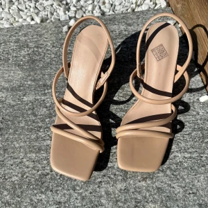 Beige sandaler med klack och tunna remmar - Säljer ett par stilrena beige sandaler från NA-KD med fyrkantig tå, tunna remmar och klack. Perfekta för dig som gillar minimalistisk design och vill ha ett par lätta skor till sommaren.