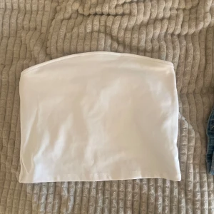 Vit tubtopp - Säljer en enkel och stilren vit tubtopp i mjukt material. Perfekt att matcha med jeans eller kjol för en fräsch look. Tubtoppen är ärmlös och har en rak passform.