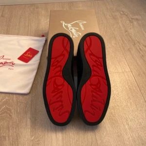 Svarta sneakers från Christian Louboutin med röd sula - Säljer ett par svarta sneakers från Christian Louboutin med ikonisk röd sula. Skorna har snörning och är tillverkade i mocka med rund tå. Kommer med originalkartong och dustbag.