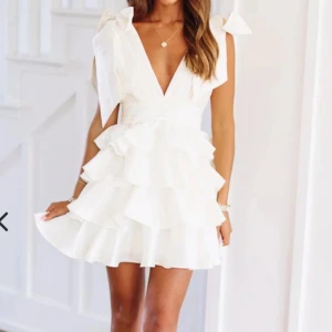 Studentklänning - Säljer en söt vit kortklänning med volanger från hazel and olive. Klänningen har en öppen rygg och knytband vid axlarna för en extra touch. Perfekt för studenten eller andra fina till fällen. Den är helt ny med lappen kvar! Säljer då jag har köpt en annan student klänning 🩷skriv vid frågor och ifall ni vill ha fler bilder