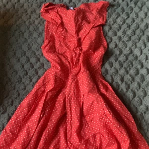 Röd prickig långklänning med volang - Säljer en röd klänning med vita prickar och volangdetaljer vid halsringningen. Klänningen har en feminin och somrig look, perfekt för varma dagar. Snygg passform och lätt material som ger ett luftigt intryck.