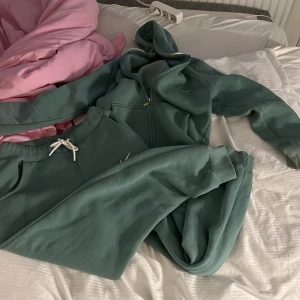 Grön hoodie från Nike med byxor - Säljer en grön hoodie m byxor från Nike med dragkedja och huva. Tröjan har långa ärmar, fickor framtill och en liten vit Nike-logga på bröstet. Perfekt för en avslappnad stil. De är i storlek l men passar mig som alltid har s, kan skicka mer bilder på de