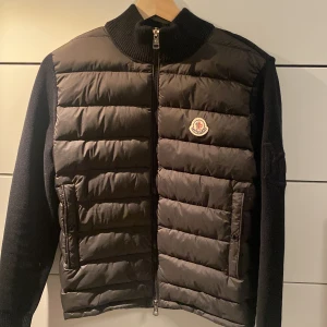 Moncler cardigan - Säljer en svart Moncler cardigan med stickade svarta ärmar. Tröjan är i storlek M och passar mellan 170-175 cm. Helt oanvänd men Inga defekter över huvud taget. Ställ frågor om det behövs, priset går att diskuteras.