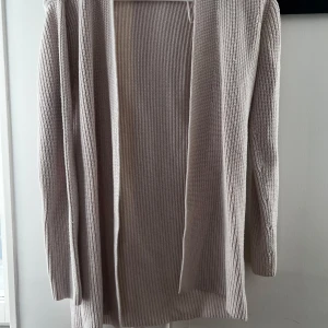 Beige stickad kofta från Lindex - Säljer en beige stickad kofta från Lindex i storlek XS. Koftan är långärmad och har en öppen front utan knappar. Perfekt att slänga på sig över en topp för en avslappnad look.