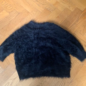 Svart fluffig tröja från Carin Wester - Mysig svart fluffig tröja från Carin Wester. Tröjan har kort ärm och är tillverkad i ett pälsliknande material som ger en cool och trendig look. Perfekt för att hålla värmen under kyliga dagar.