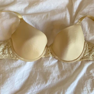 Beige bh med spetsdetaljer - Säljer en beige bh med vadderade kupor och fina spetsdetaljer på sidorna. Bh:n har justerbara axelband och slät framsida för en diskret look under kläder. Perfekt för dig som vill ha både komfort och stil.
