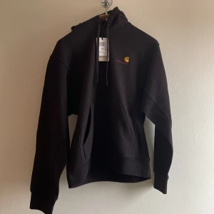 Helt ny Carhartt WIP American Script hoodie - Helt ny Carhartt hoodie med justerbar dragsko i huvan och en praktisk ficka på magen. Carhartt loggan är broderad på bröstet. Prislapp kvar, nypris ca 1400 kronor.  Luva, känguruficka, midjeresår. Material ytterskal: 80 % bomull, 20 % polyester. Material ribbstickning: 97 % bomull, 3 % elestan.  Carhartt Hooded American Script, storlek XS. Färg: svart