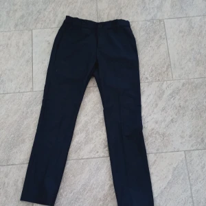 Mörkblå kostymbyxor från Lindex - Snygga mörkblå kostymbyxor från Lindex i rak modell. Byxorna har normal passform och stängs med knapp och dragkedja. Perfekta för en stilren look och passar till många tillfällen.