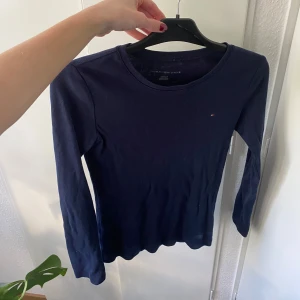 Mörkblå långärmad tröja från Tommy Hilfiger - Säljer en mörkblå långärmad tröja från Tommy Hilfiger med en liten broderad logga på bröstet. Tröjan har rund halsringning och är i ett mjukt bomullsmaterial. Perfekt basic till garderoben!