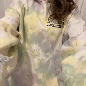 Pastellfärgad hoodie med Dua Lipa-tryck - Säljer en oversized hoodie i pastellfärgat tie-dye-mönster med texten 'Don't start now' på bröstet och stort Dua Lipa-tryck på ryggen. Hoodien har magficka och långa ärmar, perfekt för dig som gillar statement-plagg.