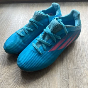 Blå fotbollsskor från Adidas - Blåa adidas fotbollsskor storlek 32. Välanvända och dubbarna är lite nedslipade men perfekta för ett barn som bara vill prova på fotboll. Sulan har inget tecken på användning, har ej formats efter foten.  