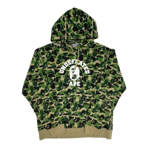 LIMITED BAPE x UNDEFEATED  - Säljer en ikonisk hoodie från A Bathing Ape x Undefeated med grönt camouflage. Perfekt för dig som gillar streetwear och vill sticka ut.