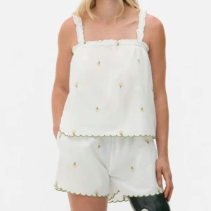 Linne set - Söt vit linnetopp med smala axelband och shorts  små broderade gula blommor. Toppen har volangkant upptill och nertill samt dekorativa vågiga sömmar i grönt. Perfekt för varma dagar. TOPP OCH SHORTS. Shorts i xs men sitter som en S mer. Oanvänd med lappar kvar 