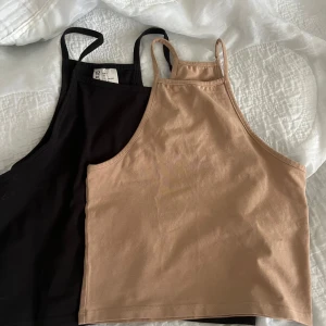 Två croppade linnetoppar i svart och beige - Säljer två croppade linnetoppar med smala axelband, en i svart och en i beige. Perfekta för sommaren och lätta att matcha med olika outfits. Den svarta är i storlek L och den beigea är i storlek S