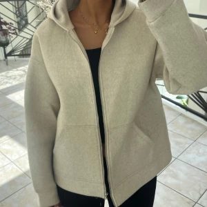 Beige hoodie/jacka med dragkedja - Säljer en beige hoodie/jacka med dragkedja och huva. Jackan har en avslappnad passform och är tillverkad i ett mjukt material. Perfekt för en chill och stilren look. Pris går att diskutera.