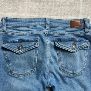 Blå bootcut jeans från Subdued - Säljer ett par blå bootcut jeans från Subdued med låg midja. Jeansen har klassiska fickor fram och bak med lock och knappdetaljer. Tillverkade i denim med snygg tvätt och markerade sömmar. 