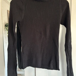 Svart ribbad polotröja från KappAhl - Säljer en svart ribbad polotröja från KappAhl i storlek S. Tröjan har lång ärm och är figurnära med klassisk polokrage. Perfekt basplagg till garderoben och enkel att matcha med olika outfits.