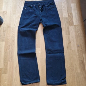 Levi's 501 svarta jeans - Klassiska svarta Levi's 501 jeans med raka ben och knappgylf. Ikonisk läderpatch bak i midjan. Perfekta för dig som gillar tidlös denimstil.