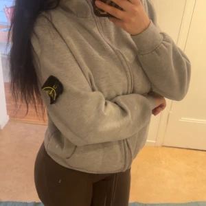 Grå ziptröja från Stone Island - Säljer en grå ziptröja från Stone Island med klassisk logga på ärmen. 