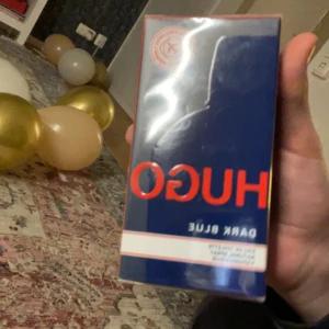 HUGO Dark Blue herrparfym - En parfym för herr från HUGO i varianten Dark Blue. Förpackningen är mörkblå med röd och vit text. Parfymen kommer i en rektangulär kartong och har en modern, stilren design.