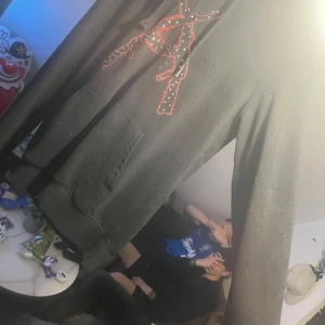 Svart hoodie med strasstenar och mönster - Säljer en svart hoodie med unikt mönster av strasstenar på bröstet, huvan och ärmslutet. Hoodien har en klassisk känguruficka och långa ärmar. Perfekt för dig som gillar detaljer och vill sticka ut. Ser smutsig ut men det är hår inte hunnit ta bort det gör det innan leverans 