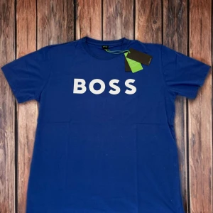 🔥💙 Helt ny! Blå t-shirt från BOSS - Snygg blå t-shirt från BOSS med vit logga tryckt på bröstet. Klassisk rund hals och korta ärmar. Perfekt för en stilren och enkel look.