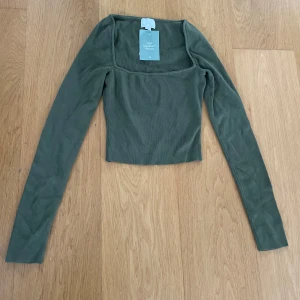 Olivgrön långärmad topp från H&M - Säljer en olivgrön långärmad topp från H&M med fyrkantig ringning. Toppen är tight och croppad, perfekt att styla med jeans eller kjol. Enkel och stilren design som passar till många tillfällen.