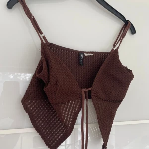 Brun croppad linnetopp från H&M - Säljer en brun croppad linnetopp från H&M med smala axelband och knyt framtill. Toppen har ett hålmönstrat tyg som ger en luftig känsla, perfekt för varma dagar. Snygg och trendig modell som passar till mycket.