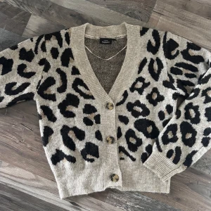 Leopardmönstrad kofta från KappAhl - Säljer en beige kofta från KappAhl med svart leopardmönster. Koftan har v-ringning, knappar framtill och ribbade muddar vid ärmslut och nederkant. Aldrig använt