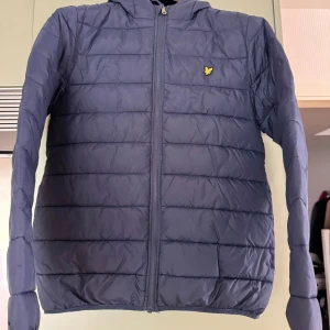 Blå pufferjacka från Lyle & Scott Junior - Säljer en blå pufferjacka från Lyle & Scott Junior 14/15 år (XS/S senior) med huva. Jackan har quiltad design och en liten gul logga på bröstet. Perfekt för kyligare vårdagar. Pris kan diskuteras.