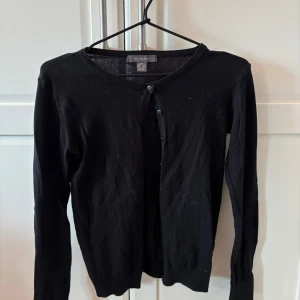 Svart kofta från Primark - En klassisk svart kofta från Primark i tunnare material. Koftan har rund halsringning, långa ärmar och knäppning framtill med små svarta knappar. Perfekt att slänga över en topp eller klänning.