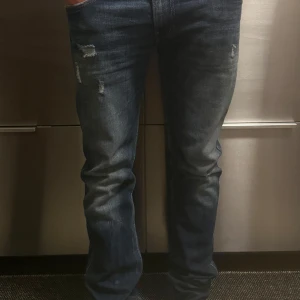 Replay jeans - Säljer ett par mörkblå jeans med slitningar på låret och knät. Jeansen har klassisk femficksdesign och raka ben. Perfekta för en avslappnad stil och passar till det mesta i garderoben.