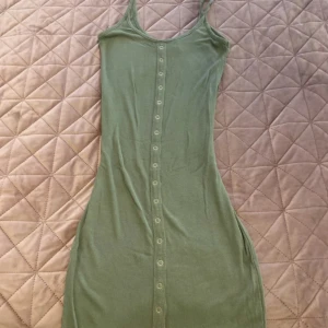 Grön ribbad kortklänning Bik Bok XS - Skick: Bra Storlek: Xs Material: bomull.                                                Märke: bikbok                                                           grön ribbad klänning från Bik Bok i storlek XS. Modellen är ärmlös med smala axelband och har knappar längs hela framsidan. Materialet är mjukt och stretchigt, perfekt för varma dagar. Enkel och stilren design som är lätt att matcha med sneakers eller sandaler.