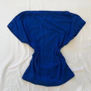 Blå kortärmad topp med öppen rygg - Snygg blå topp med korta ärmar och en cool öppen rygg. Modellen har en rundad halsringning. Perfekt för dig som gillar att sticka ut med en enkel men ändå unik stil. Materialet är mjukt och känns skönt mot huden. 💞