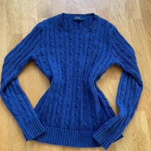 Blå kabelstickad tröja Polo Ralph Lauren - Kabelstickad blå tröja från Polo Ralph Lauren med rund halsringning och långa ärmar. Klassisk och tidlös 